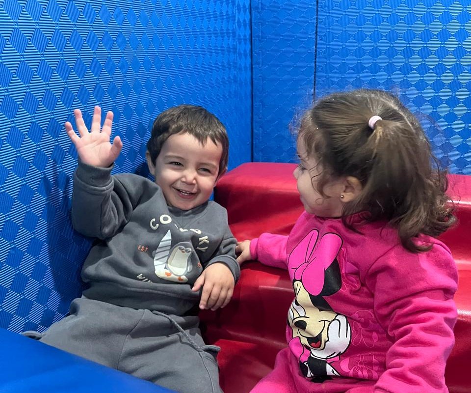 Un niño saluda con la mano junto a una compañera